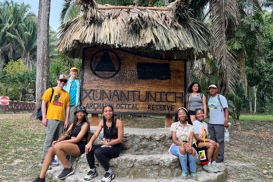 students and faculty stand next to a wooden sign