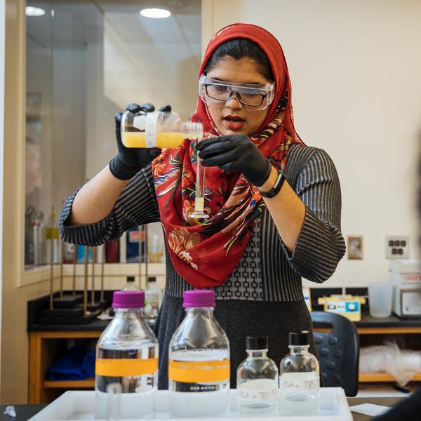 A 化学主要 student wearing a colorful hijab pours a solution into a test tube.