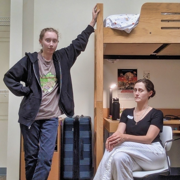 a mother and daughter lean up against a wooden bunk bed in a college dormitory
